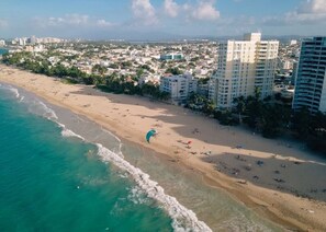 An aerial view of a beach with a parasail, buildings, and a coastline.