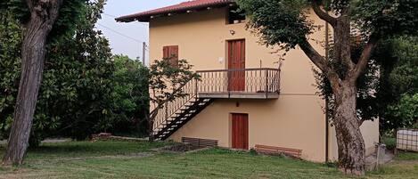 A two-story building with a red-tiled roof, a balcony with a wrought-iron railing, and a staircase leading to the upper floor.