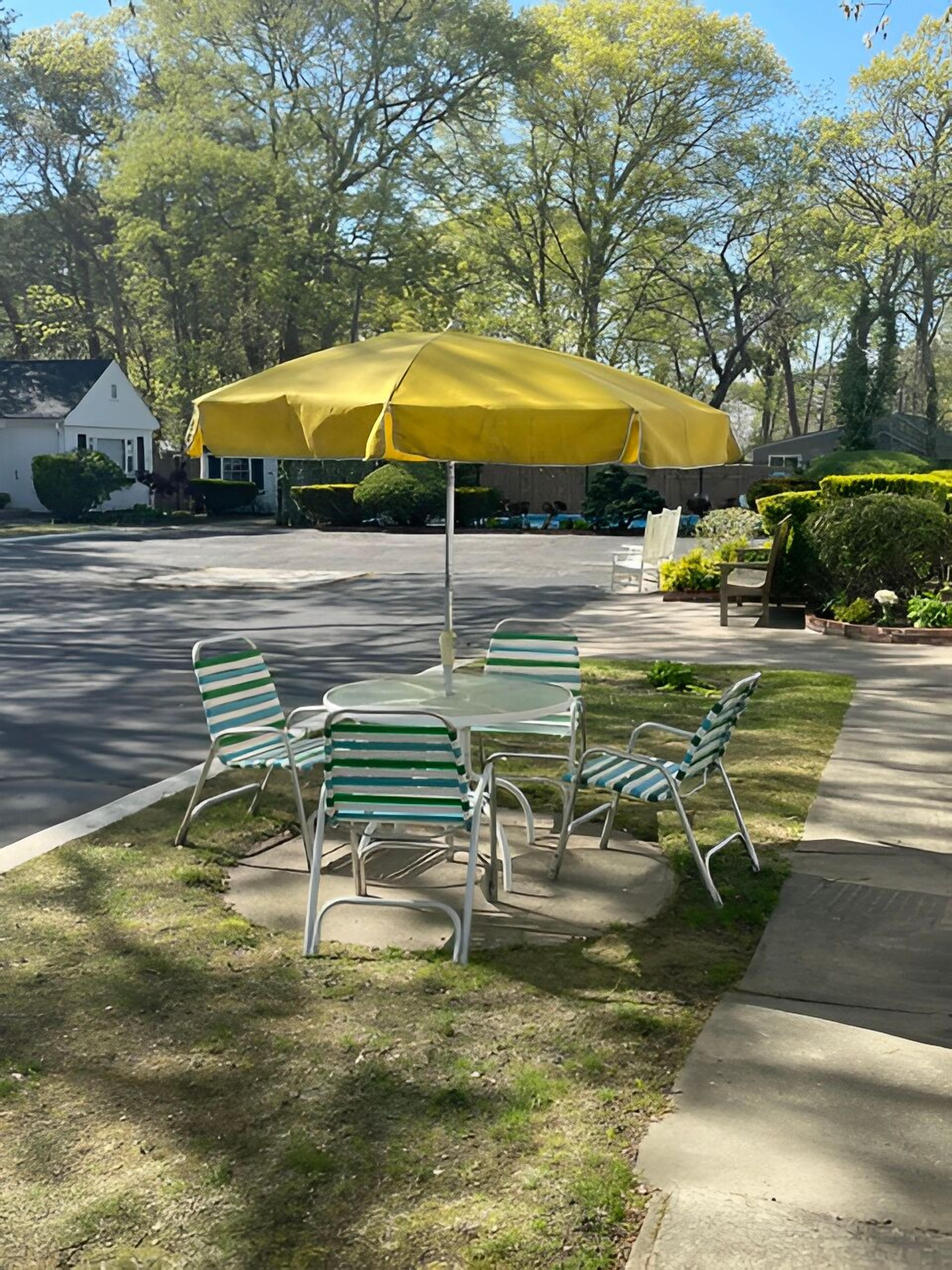 A patio with a yellow umbrella, metal chairs, and a table.