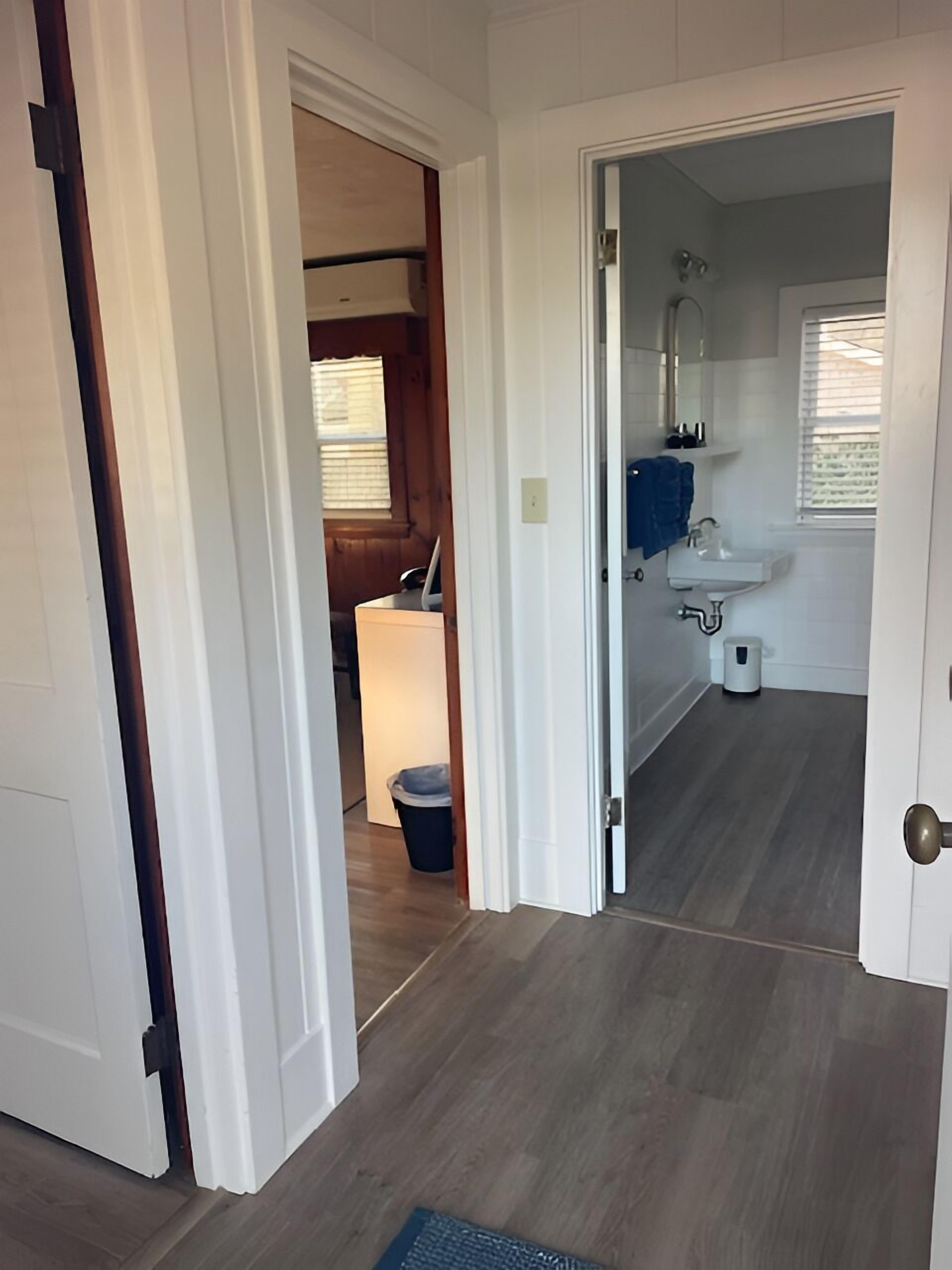 A hallway leading to a bathroom with a sink, mirror, and window.
