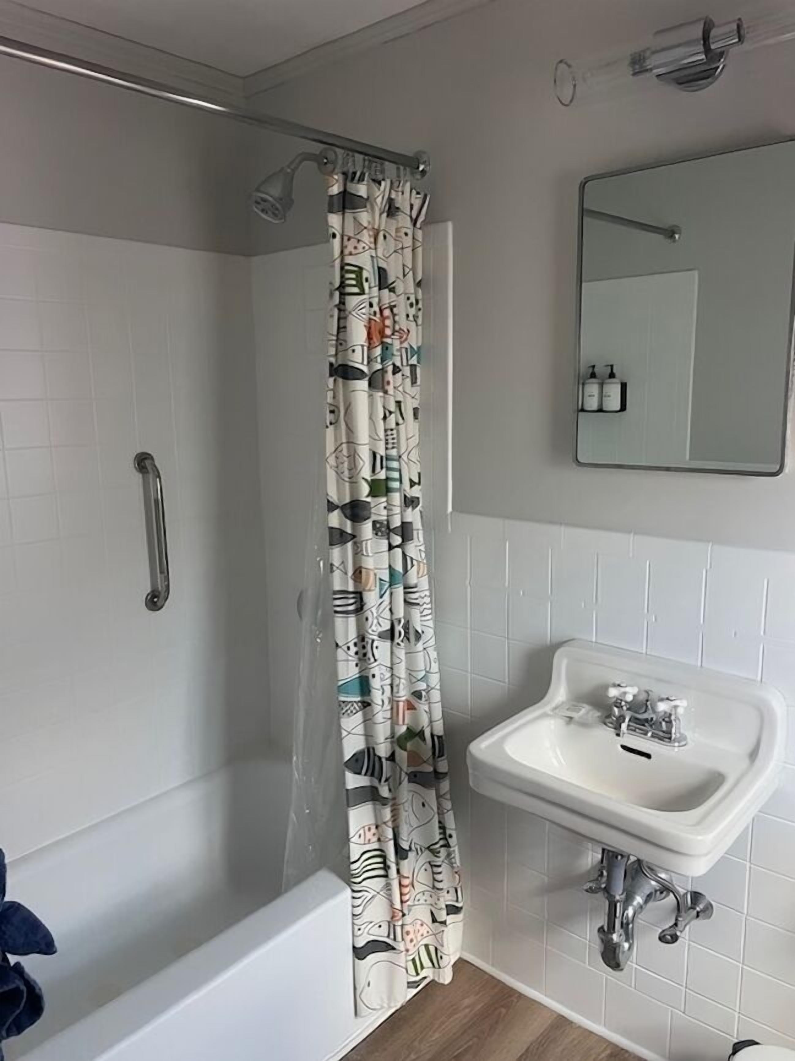 Een badkamer met een douche, een handgreep, een wastafel en een spiegel.