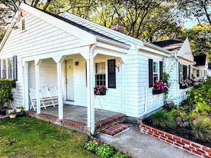 A white single-story house with a porch, a brick foundation, and flower boxes. - Cape Cod Motor Inn (South Yarmouth)