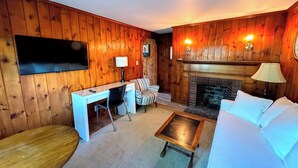 Habitación con paneles de madera, televisor, escritorio, silla, sofá y chimenea.