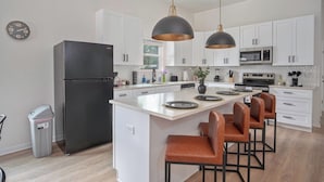 A modern kitchen with white cabinets, a black refrigerator, a central island with bar stools, and pendant lighting. - Generous 4br/3ba Charmer Near Glorius Downtown! (San Antonio)