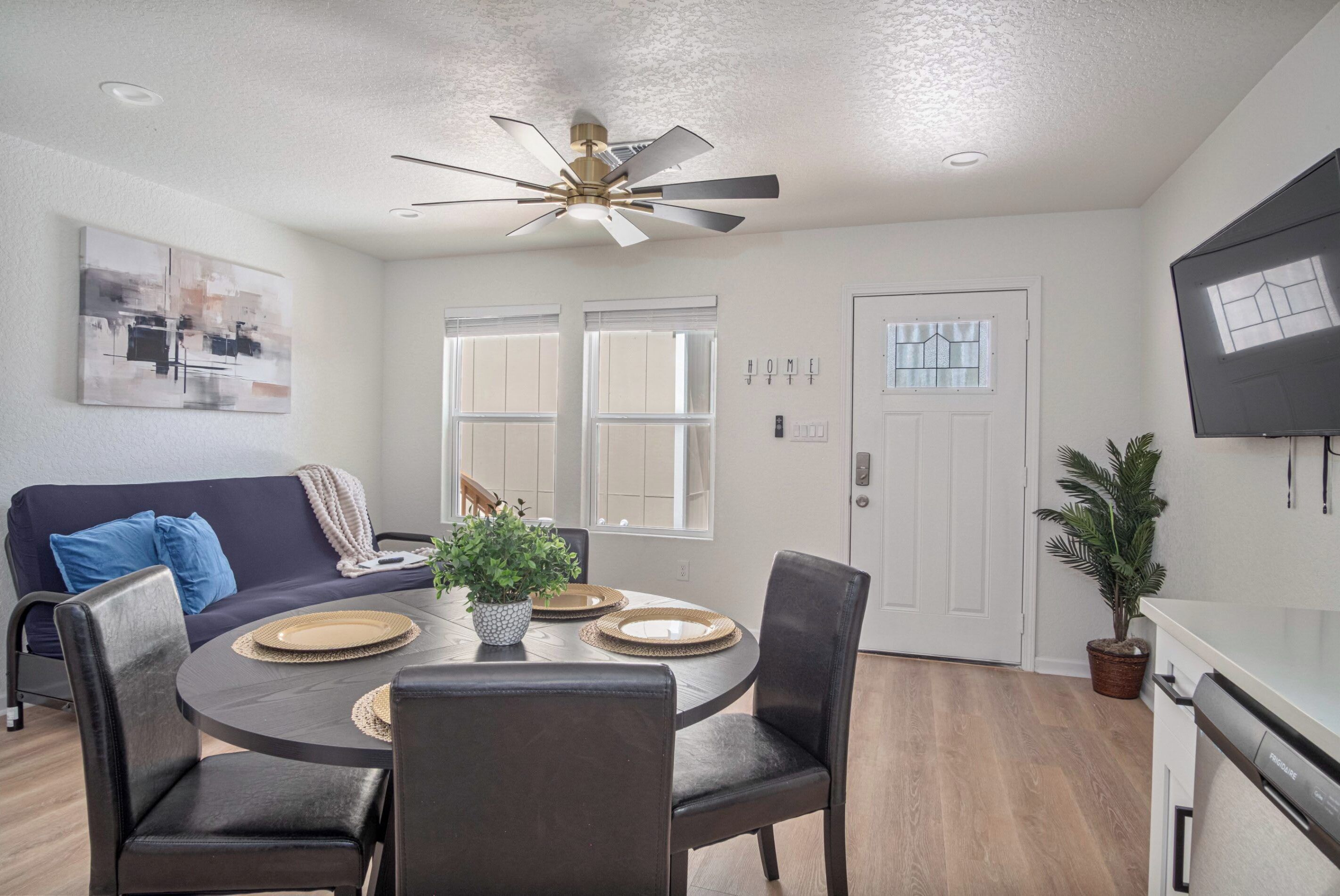 A dining area with a round table, black chairs, a ceiling fan, and a potted plant.