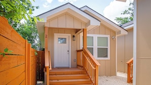 A house with a wooden front door, a small porch with steps, and a window. - Historic Comfort 2BR/1BA Guesthouse Near Riverwalk (San Antonio)