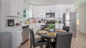A modern kitchen with white cabinets, stainless steel appliances, and a dining area with black chairs and woven placemats. - Historic Comfort 2BR/1BA Guesthouse Near Riverwalk (San Antonio)
