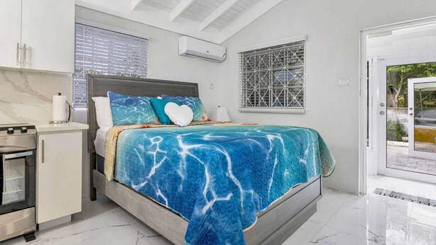 A bedroom with a bed, a small kitchenette, and a sliding glass door to the outside. - Coastal Pleasures Studio (Saint Ann's Bay)