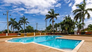 A rectangular swimming pool with a tiled deck, surrounded by palm trees and a clear sky. - Coastal Pleasures Studio (Saint Ann's Bay)
