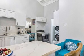 A compact kitchen with white cabinets, a marble countertop, and a blue sofa.