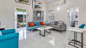 Ein geräumiges Wohnzimmer mit Deckenventilator, blauem Sofa, grauem Sofa und weißem Couchtisch.