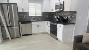 A modern kitchen with white cabinets, stainless steel appliances, a microwave, and a coffee maker. - One bedroom house (Portland)