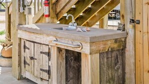 A rustic wooden outdoor kitchen with a sink and faucet, a fire extinguisher, and a hose. - Charming Studio house with WiFi & AC in brilliant Holly Beach, La (Cameron)