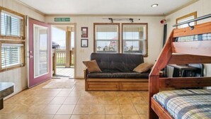 A room with a wooden bench, a sofa, and a bunk bed. There is a door leading outside and a window with blinds. - Charming Studio house with WiFi & AC in brilliant Holly Beach, La (Cameron)