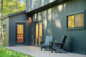A modern building with a dark exterior, a sliding glass door entrance, and a patio area with two chairs and a table. - Luxury Scandinavian nature escape, private saun (Springfield)