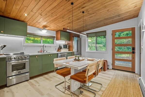 A modern kitchen with green cabinets, stainless steel appliances, and a dining area with a white table and brown chairs. - Luxury Scandinavian nature escape, private saun (Springfield)