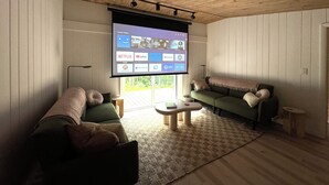A cozy living room with a large TV screen displaying streaming services, a green sofa, a small coffee table, and a wooden ceiling.