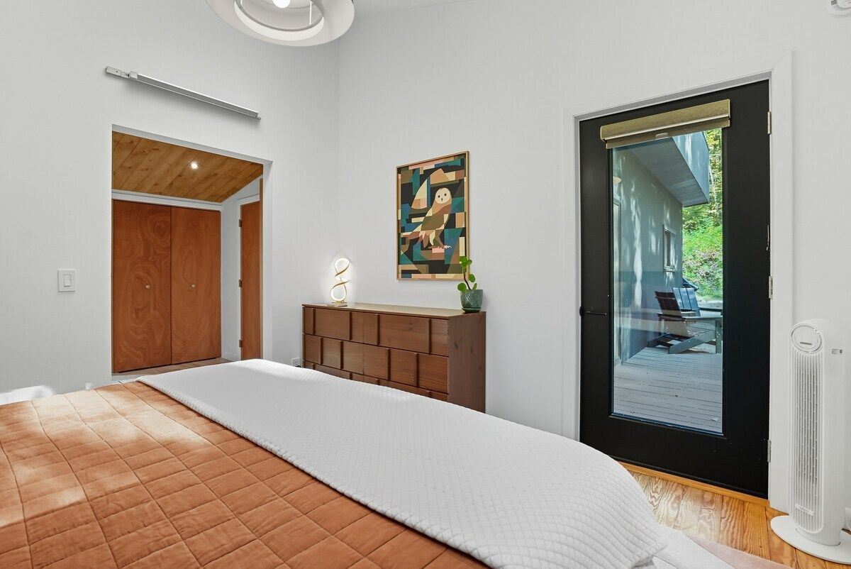 Een slaapkamer met een bed, een dressoir, een schilderij, een deur naar een balkon en een plafondlamp.