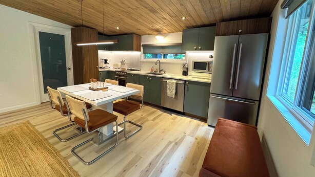 A modern kitchen with wooden ceiling, stainless steel appliances, and a dining area with a table and chairs.