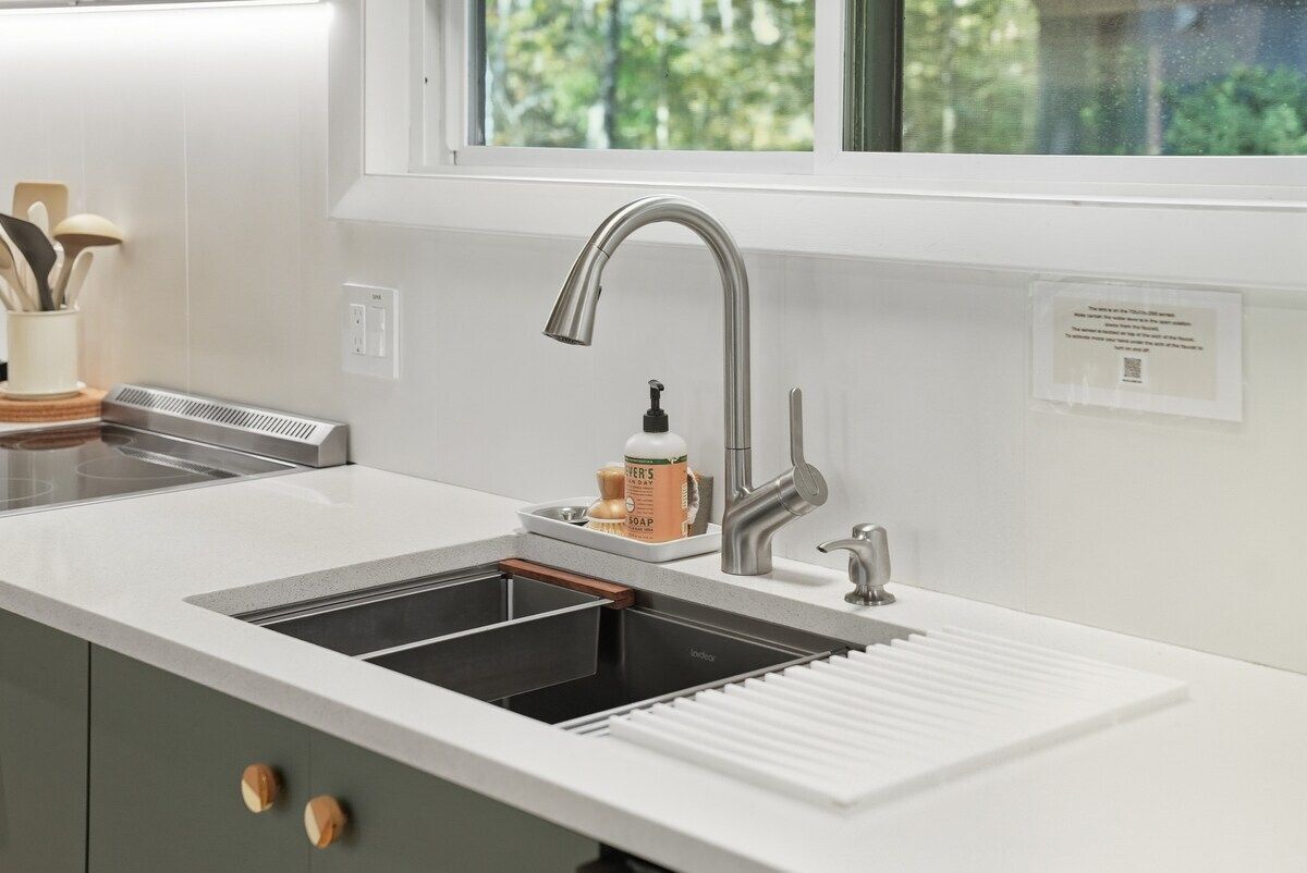 Een moderne keuken met een roestvrijstalen spoelbak, een inbouwoven en een raam boven de spoelbak.
