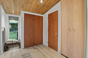 A room with a wooden ceiling, a bench with cushions, and a large wooden wardrobe.