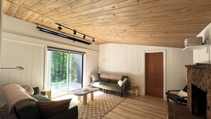 A cozy living room with a wooden ceiling, a fireplace, a sofa, a coffee table, and a large sliding glass door leading to a deck.