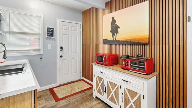 Eine kleine Küche mit Mikrowelle und Toaster auf einem Holzschrank, eine Tür mit einem Willkommensschild und ein Wandbild von einem Sonnenuntergang.