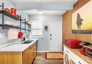 A compact kitchen with wooden cabinets, a white countertop, a red microwave, and a wall-mounted oven. - Vibrant Cowgirl Hideaway - Rodeo Themed, Fire Pit & 1/2 mile walk to Whiskey Row (Prescott)