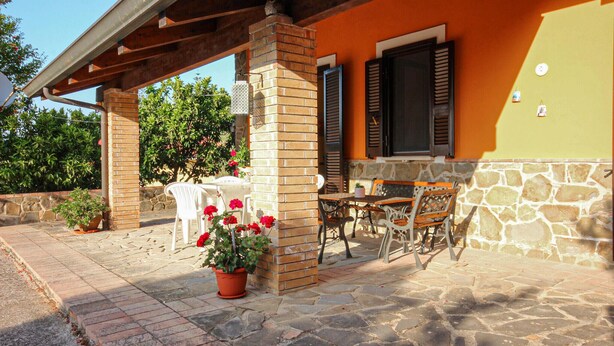 An outdoor patio with a stone floor, a brick column, a table with chairs, and a potted plant with red flowers. - Gorgeous home in Perdifumo with WiFi (Perdifumo)