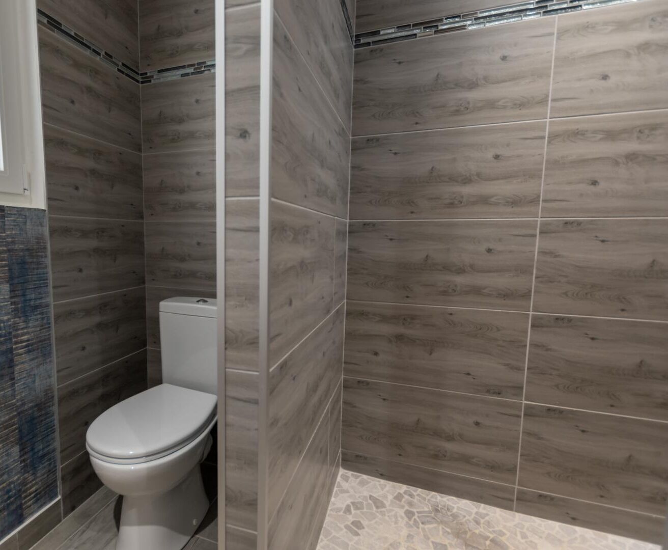 A bathroom with a toilet, a shower area, and tiled walls.