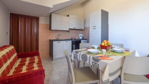 A compact living space with a kitchenette, a dining area with a table set for two, and a red sofa. - 1 bedroom amazing apartment in Acquedolci (Acquedolci)