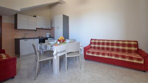 A compact living space with a dining table, chairs, a red sofa, and a kitchenette. - 1 bedroom amazing apartment in Acquedolci (Acquedolci)