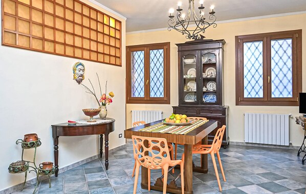 A dining area with a wooden table, orange chairs, a chandelier, a cabinet with dishes, and a window with a lattice design. - Awesome apartment in Menfi with WiFi (Menfi)