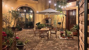 Terrassa a l'aire lliure amb taula i cadires, envoltada de plantes en testos i llums penjants.