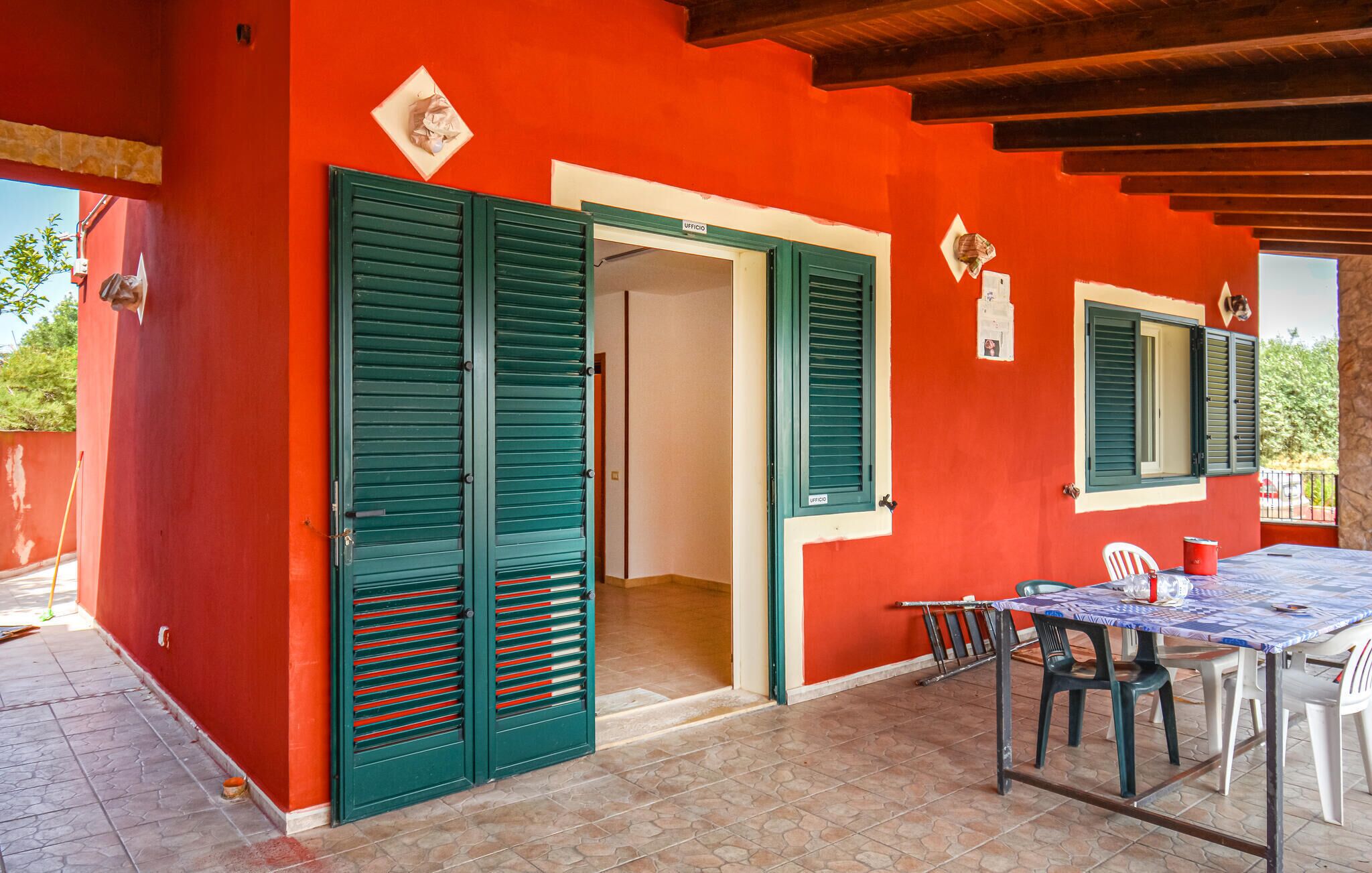 Un edificio rosso con persiane verdi, un patio piastrellato e un tavolo con sedie.