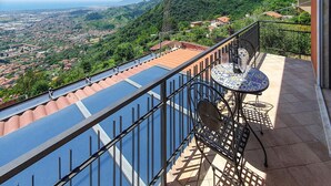 Un balcón con vistas a un pueblo costero, una mesa de baldosas y una barandilla de metal.