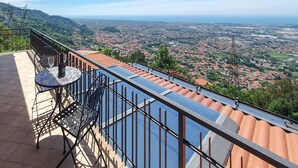 Un balcón con mesa y sillas, con vista a un paisaje urbano con edificios y vegetación.