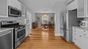 A modern kitchen with stainless steel appliances, a dining area with wooden chairs, and a chandelier. - Arcade Games, Pool Table, Huge Deck, Seasonal View (Davenport)