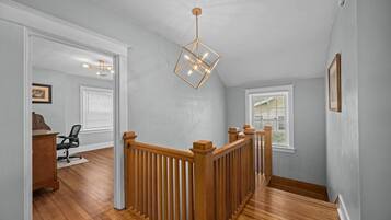 Un hall spacieux doté d’un plancher en bois, d’une rambarde en bois et d’un luminaire suspendu aux formes géométriques.