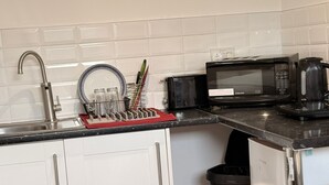 A compact kitchen with white cabinets, a stainless steel sink, a microwave, and a small trash bin. - Cosy Adorable 1 Bedroom Studio in London (London)