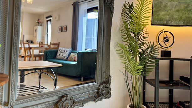 Un espejo refleja un salón con un sofá verde, una mesa de comedor y una planta en maceta.