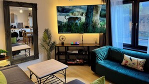 Una sala de estar con un televisor de pantalla plana grande, un sofá, una mesa de comedor y un espejo.