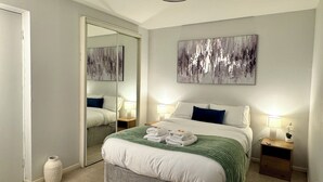 A modern bedroom with a large bed, two bedside tables with lamps, a mirror, and abstract wall art. - Stylish & Spacious City-Centre Flat | Prime Location, PS5, Netflix, Dining Space (Edinburgh)