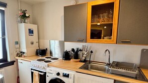 A compact kitchen with a built-in oven, microwave, and washing machine. It includes a sink, a countertop with various kitchen items, and a cabinet above the sink. - Stylish & Spacious City-Centre Flat | Prime Location, PS5, Netflix, Dining Space (Edinburgh)