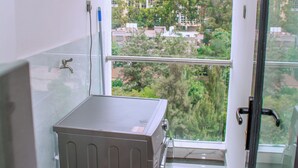 Ein schmaler Balkon mit Warmwasserbereiter, einer Glastür und Blick auf Gebäude und Bäume.
