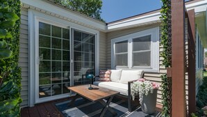 A covered patio with a wooden table, a white sofa, and a potted plant.