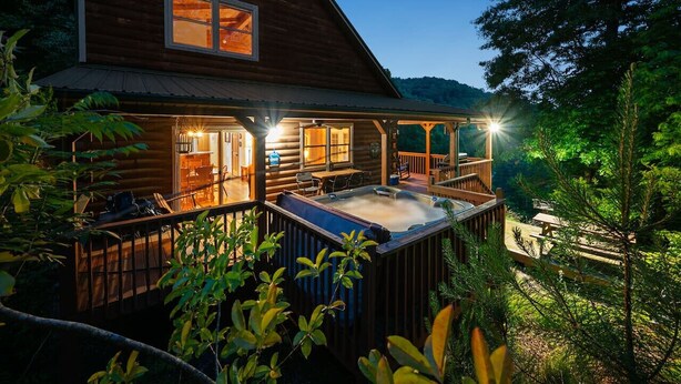 Eine Blockhütte mit Whirlpool auf einer Terrasse, umgeben von Bäumen.