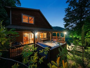 Eine Blockhütte mit Whirlpool auf einer Terrasse, umgeben von Bäumen.