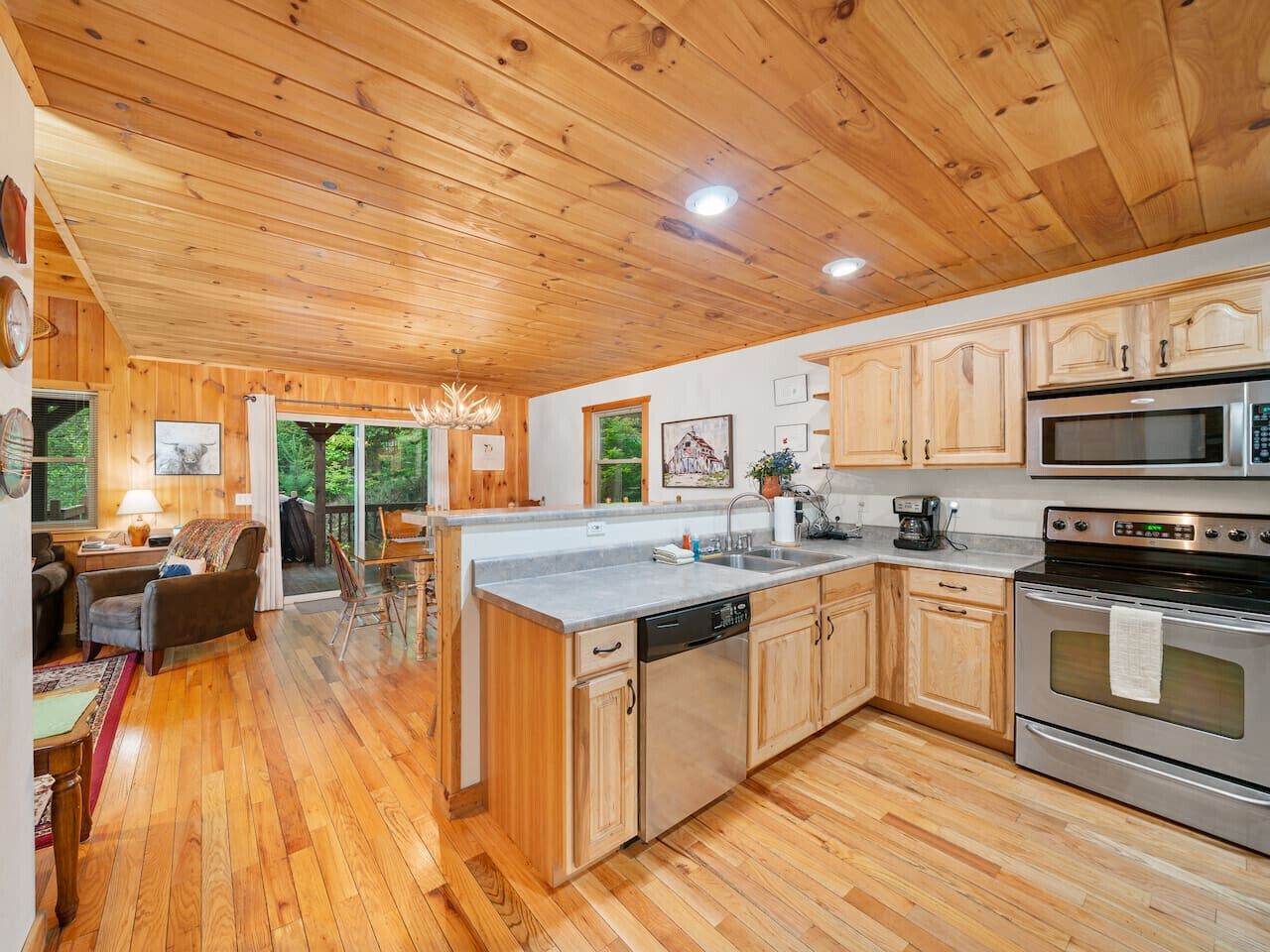 A wooden-paneled kitchen with a central island, stainless steel appliances, and a view to the outdoors.