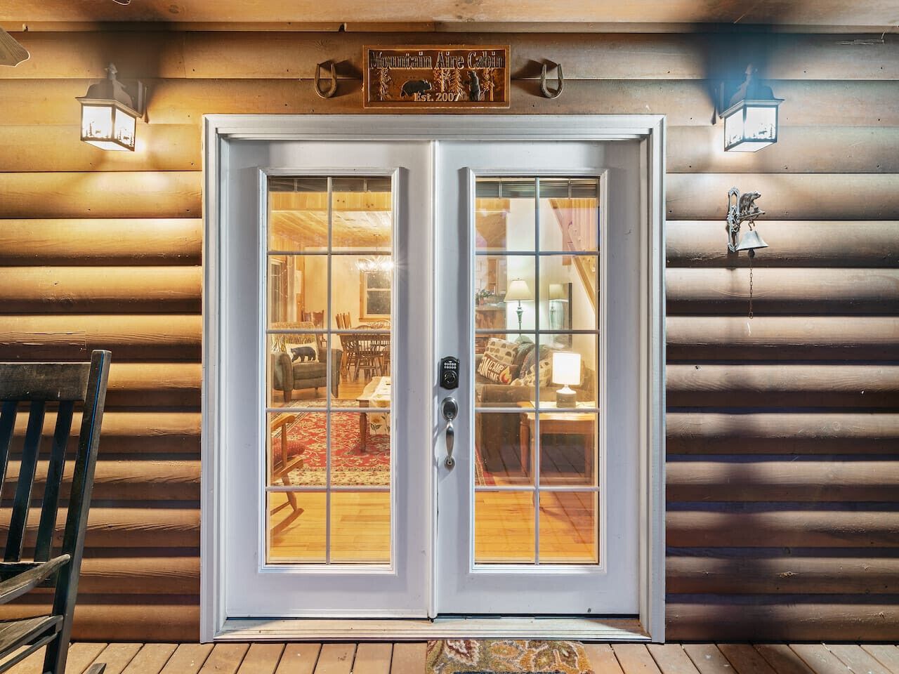 A wooden cabin with a white-framed glass door, a sign above it, and two wall-mounted lanterns.